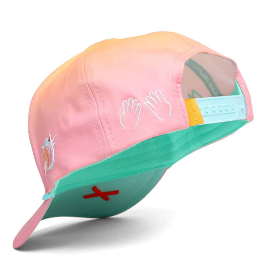 Side-back view of the peach-pink gradient cap showing embroidered hand icons, a teal snapback closure, and a small orange X embroidery on the underside.