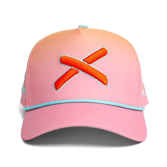 Front view of the peach-pink gradient baseball cap with a prominent orange X logo centered above the teal-trimmed brim.