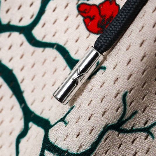 Close-up of a silver clasp on a black cord against the textured beige shorts with green branches and a red flower