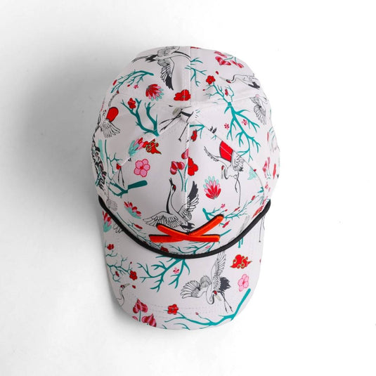 “Top-down angled view of the floral and bird-pattern baseball cap with orange X logo on the brim.”