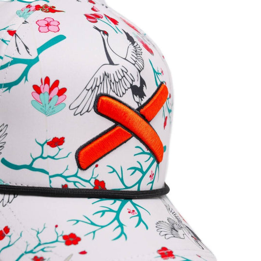 “Close-up side view of the cap showing the orange X patch and detailed floral crane print.”