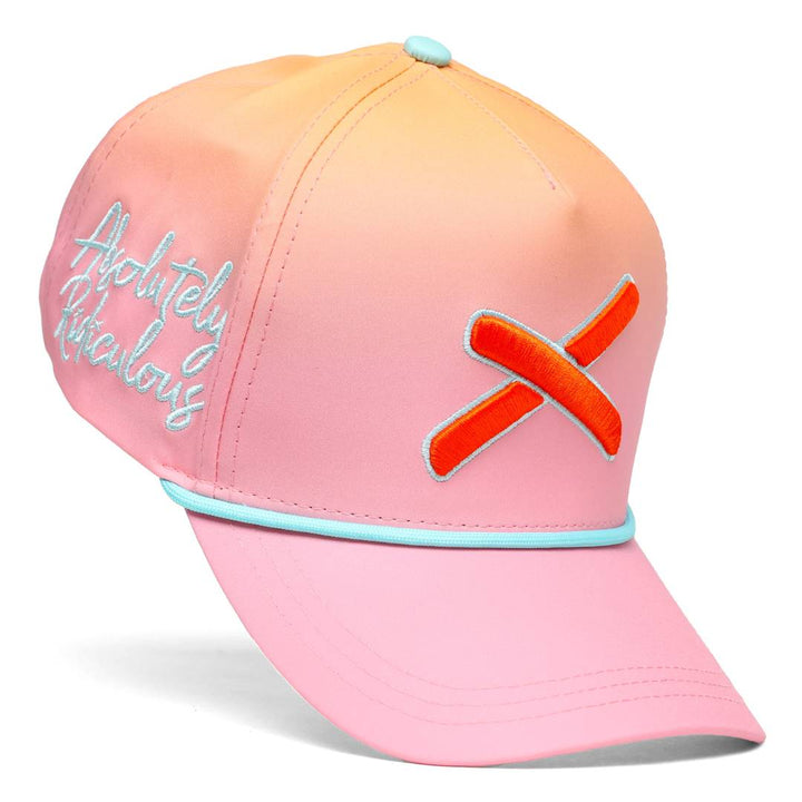 Angled view of a peach-pink gradient baseball cap featuring teal trim, embroidered script on the front left panel, and a bold orange X logo on the side.